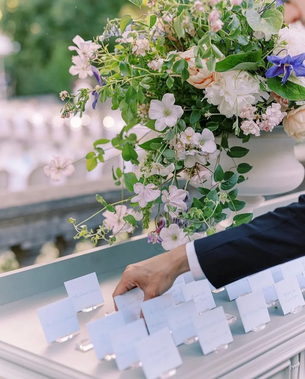 A hand placing name cards beside a tall arrangement of pink and white flowers
